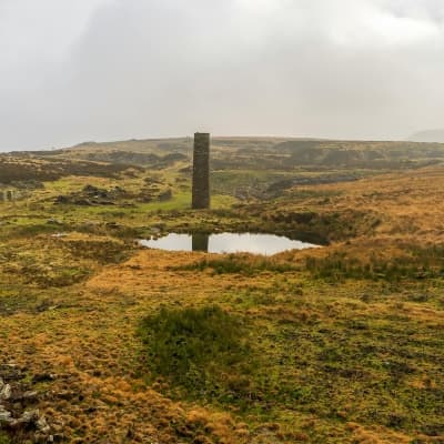 Peatland grass covered moor with small pool of water and stone tower